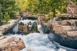 Group of riders in a colorful boat on a rocky water ride, splashing through a narrow canal.