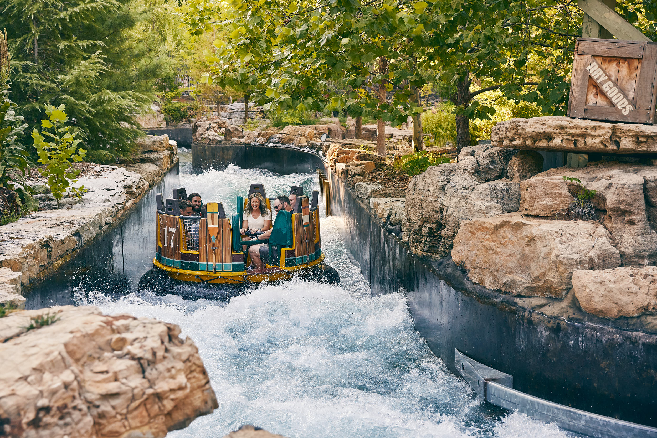Group of riders in a colorful boat on a rocky water ride, splashing through a narrow canal.