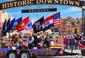 Float in a parade under a Historic Downtown arch, with US flags and veterans' banners on the float.