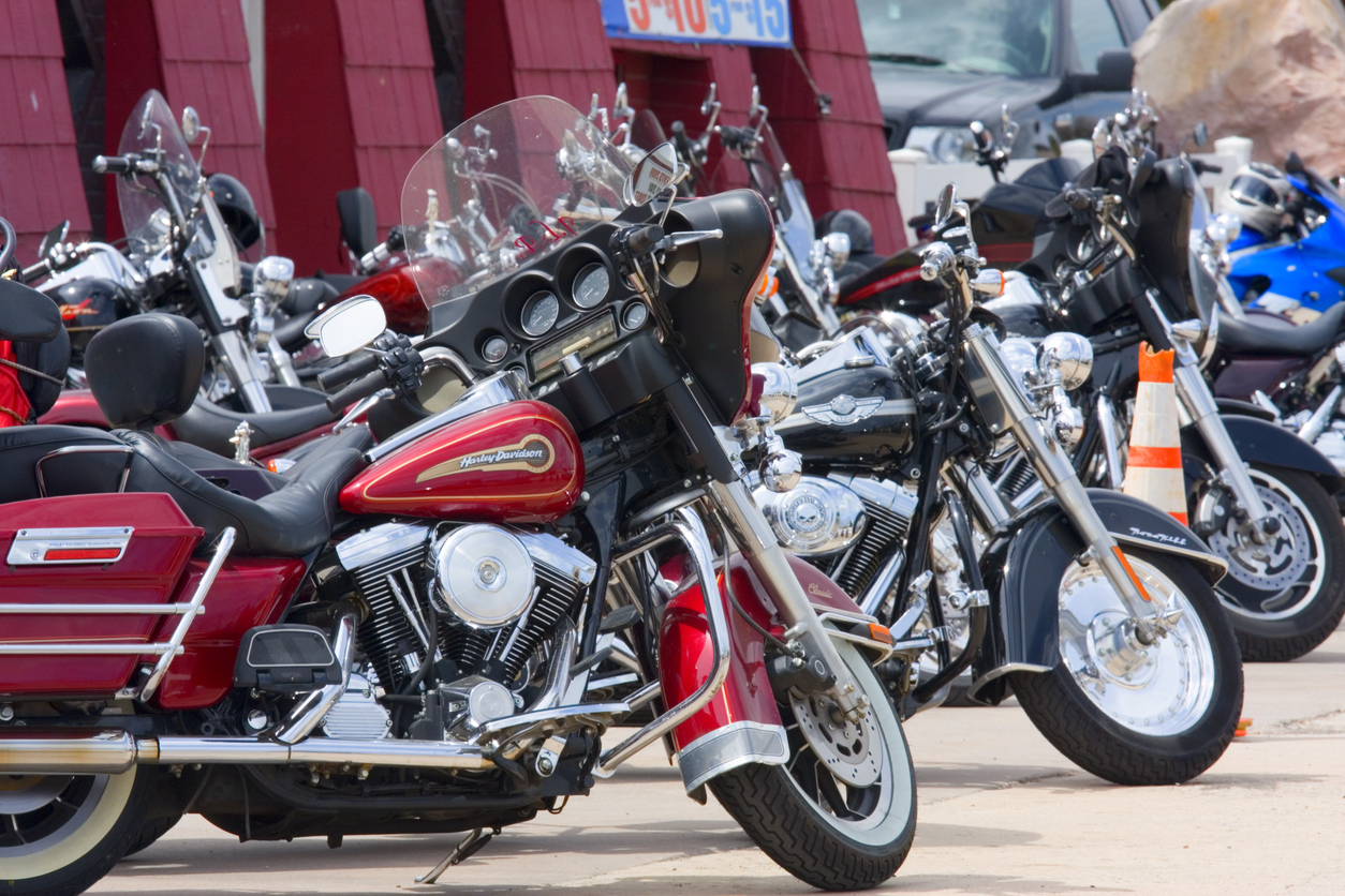 Row of parked motorcycles in a lot, foreground red Harley‑Davidson with windshield and saddlebags.