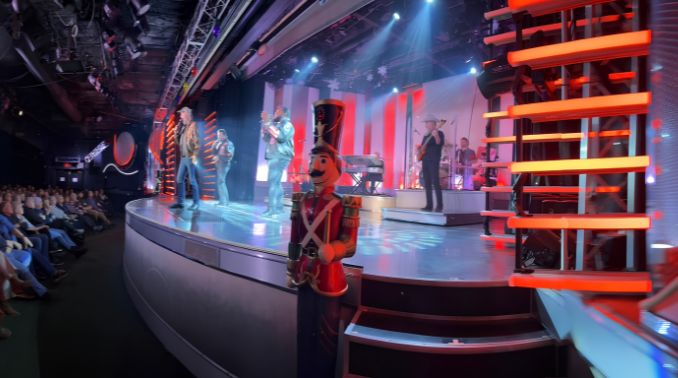 Stage performance with musicians and dancers on a curved platform; a life-size nutcracker statue stands at the edge while the audience watches from the left.
