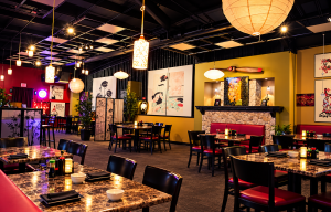 Asian-inspired restaurant interior with marble tables, black chairs with red cushions, warm hanging lanterns, and potted plants.
